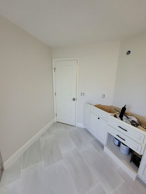 Renovated kitchen corner with white cabinets, door, light gray walls, and tiled floor