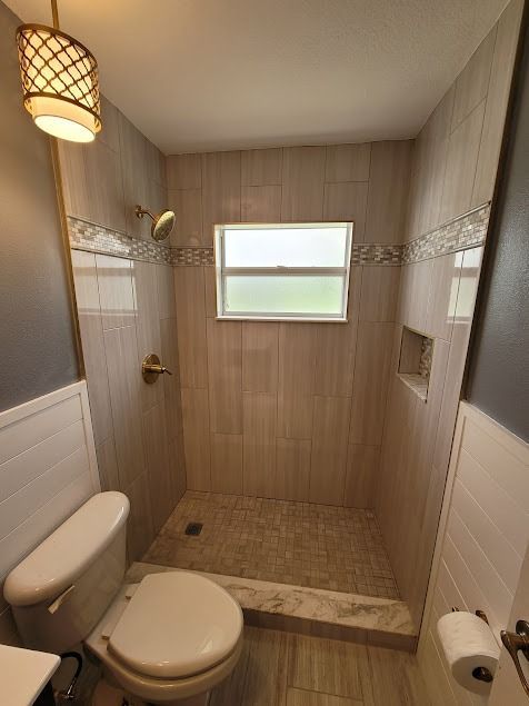 Small bathroom with beige tiled shower, toilet, and window