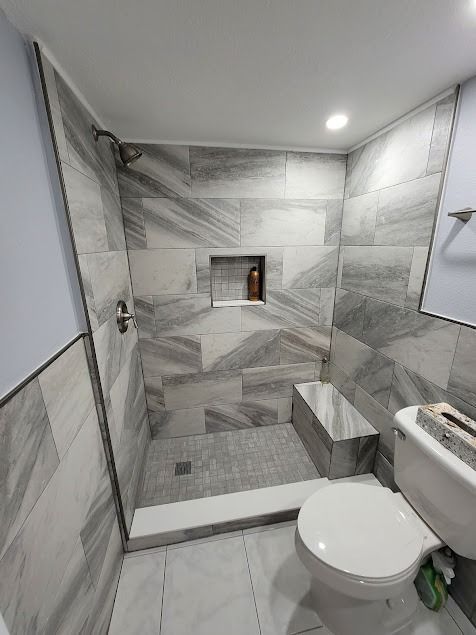 Bathroom with gray tiled shower, bench, and toilet; gray and white tiles