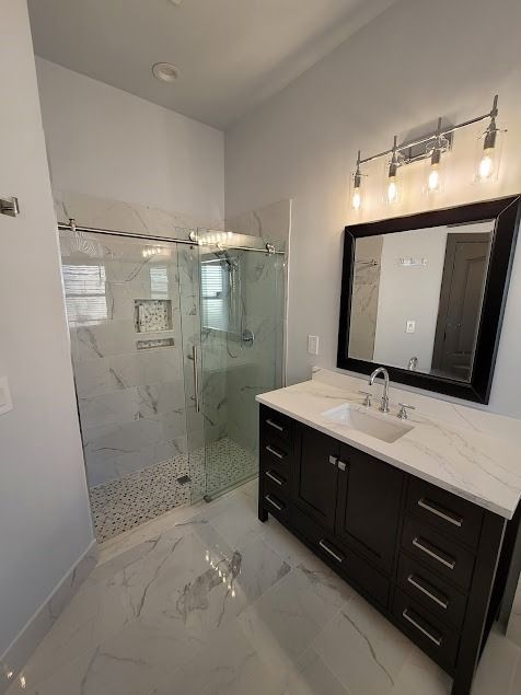 Modern bathroom with marble tile, dark vanity, glass shower, and a large mirror