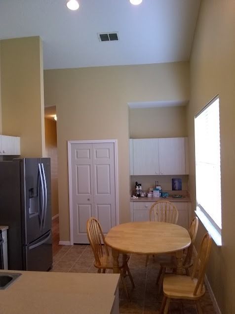 A kitchen with a refrigerator, table, chairs, pantry door, and upper cabinets on a tan-colored wall