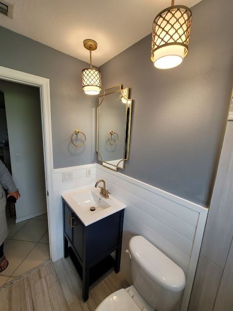 Bathroom with blue vanity, white toilet, gold accents, gray walls, and white tile wainscoting