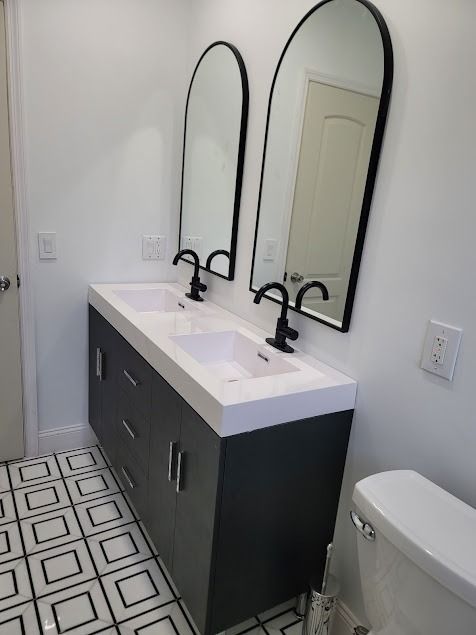 Modern bathroom with floating gray double vanity, arched black mirrors, white countertop, and patterned tile floor