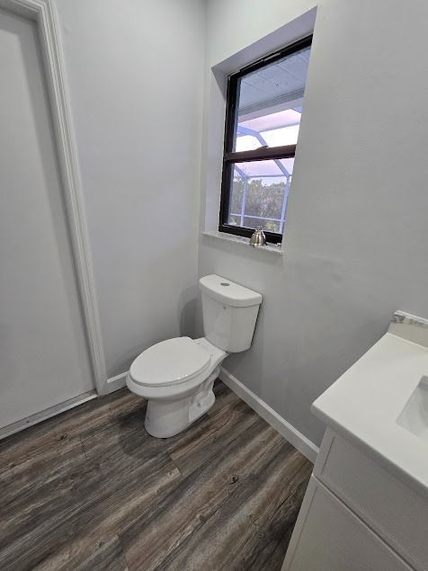 White toilet in a bathroom with a window above it and wood-look flooring