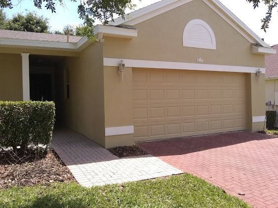 Tan house with a beige garage door and red brick driveway