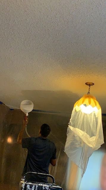 Person spraying paint on a ceiling, light fixture covered, room interior, yellow paint