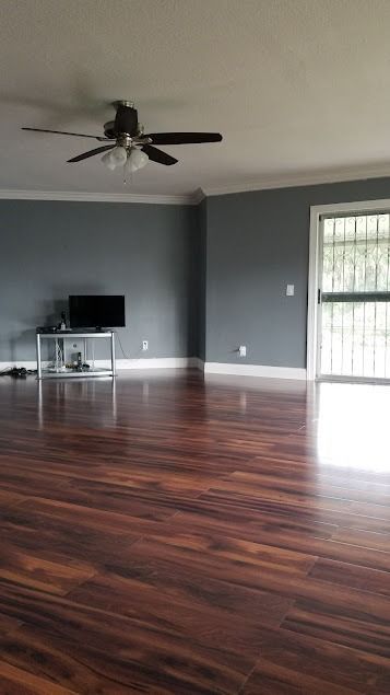 Empty living room with dark gray walls, dark wood floor, TV on a stand, and ceiling fan