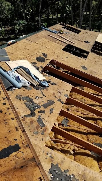 Rooftop with exposed wooden beams, insulation, and sections of torn roofing material, likely undergoing repairs