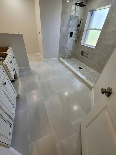 Bathroom with light gray tiled floor, walk-in shower, white vanity, and window
