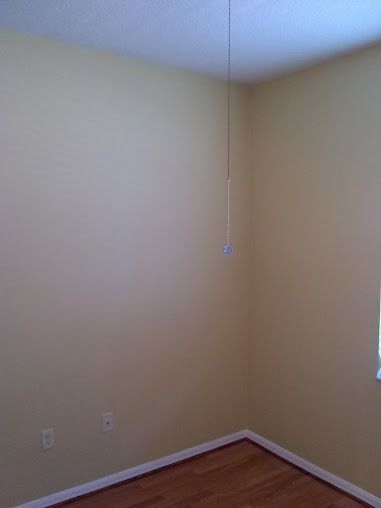 Empty room with light yellow walls, wooden floor, and a ceiling fan pull cord