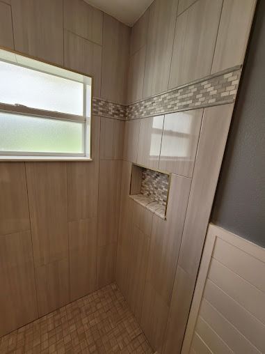 Tiled shower with light-colored walls, a window, built-in shelf, and accent tile border