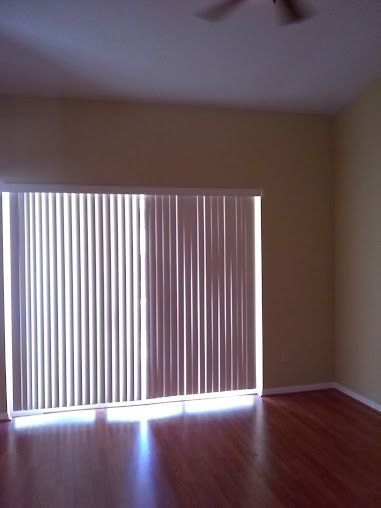 A room with vertical blinds on a sliding glass door, hardwood floor, and beige walls