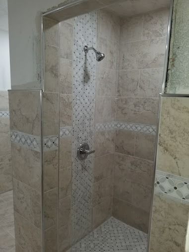 Tiled shower with a decorative central strip, a showerhead, and silver fixtures