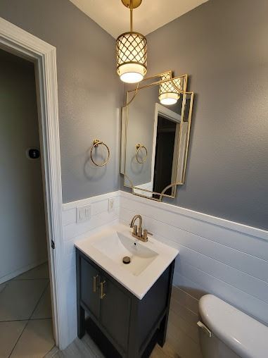 Bathroom with gray walls, gold accents, vanity, mirror, and pendant light