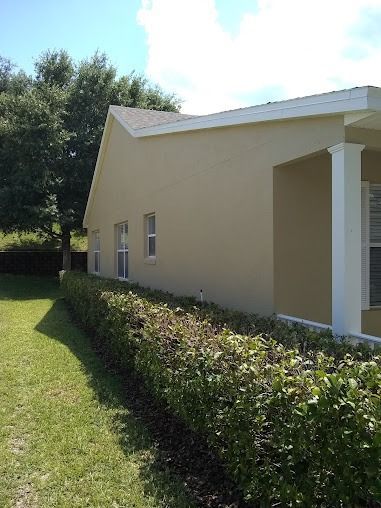 Beige house with white trim and columns, next to green lawn and a hedge