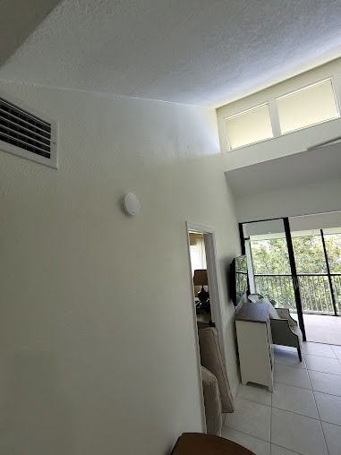 Interior view of a room with high ceilings, a white wall with a smoke detector, and a doorway