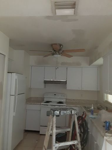 White kitchen with cabinets, appliances, and a ceiling fan; ladder in foreground