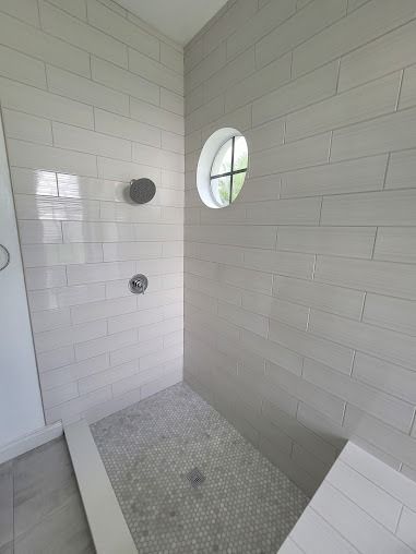 A tiled shower stall with a pebble floor, circular window, and shower fixtures