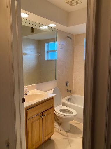 Bathroom with a sink, toilet, and bathtub; tan tiles and light wood cabinets