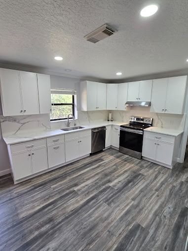 White kitchen with gray-wood flooring, white countertops, stainless steel appliances, and a window