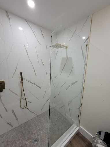 Modern shower stall with white marble-like tiles, glass door, and gold fixtures