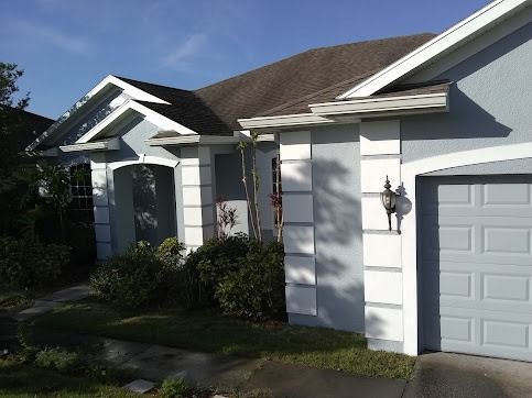Blue house with white trim, garage, bushes, and a blue sky