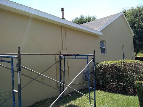 Tan house exterior with scaffolding, window, and green bushes