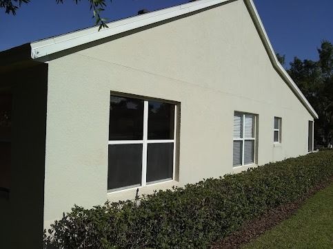 Beige house with white-framed windows and a hedge row, under a sunny sky