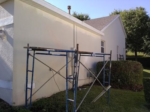 Scaffolding against a light-colored house exterior, with a grassy lawn and bushes