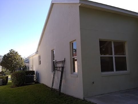 Exterior of a house with light beige stucco walls, windows, and green lawn under a blue sky