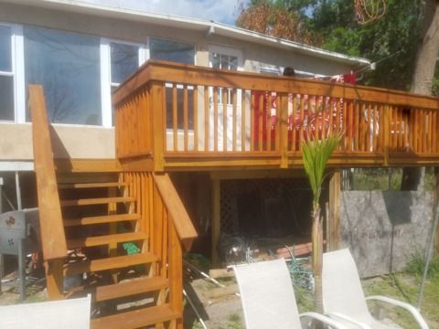 Wooden deck with stairs, overlooking a yard with white chairs