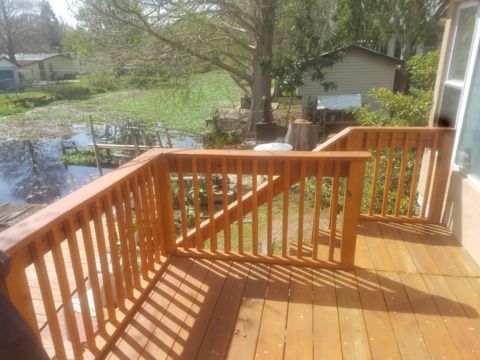 Wooden deck with railing overlooking a body of water and vegetation, sunny day