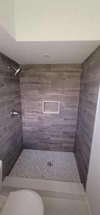Bathroom shower stall with gray wood-look tiles, mosaic floor, and recessed shelf