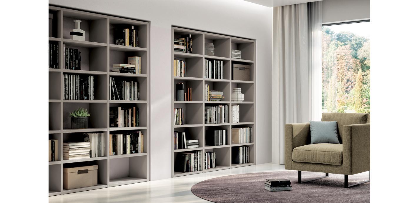 Librerie incassate in una parete, piene di libri e decorazioni, accanto a una finestra e a una poltrona.