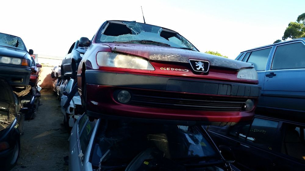 A red Peugeot 306 car in a junkyard, stacked on top of other vehicles. — Crypto Parts In Tuggerah, NSW