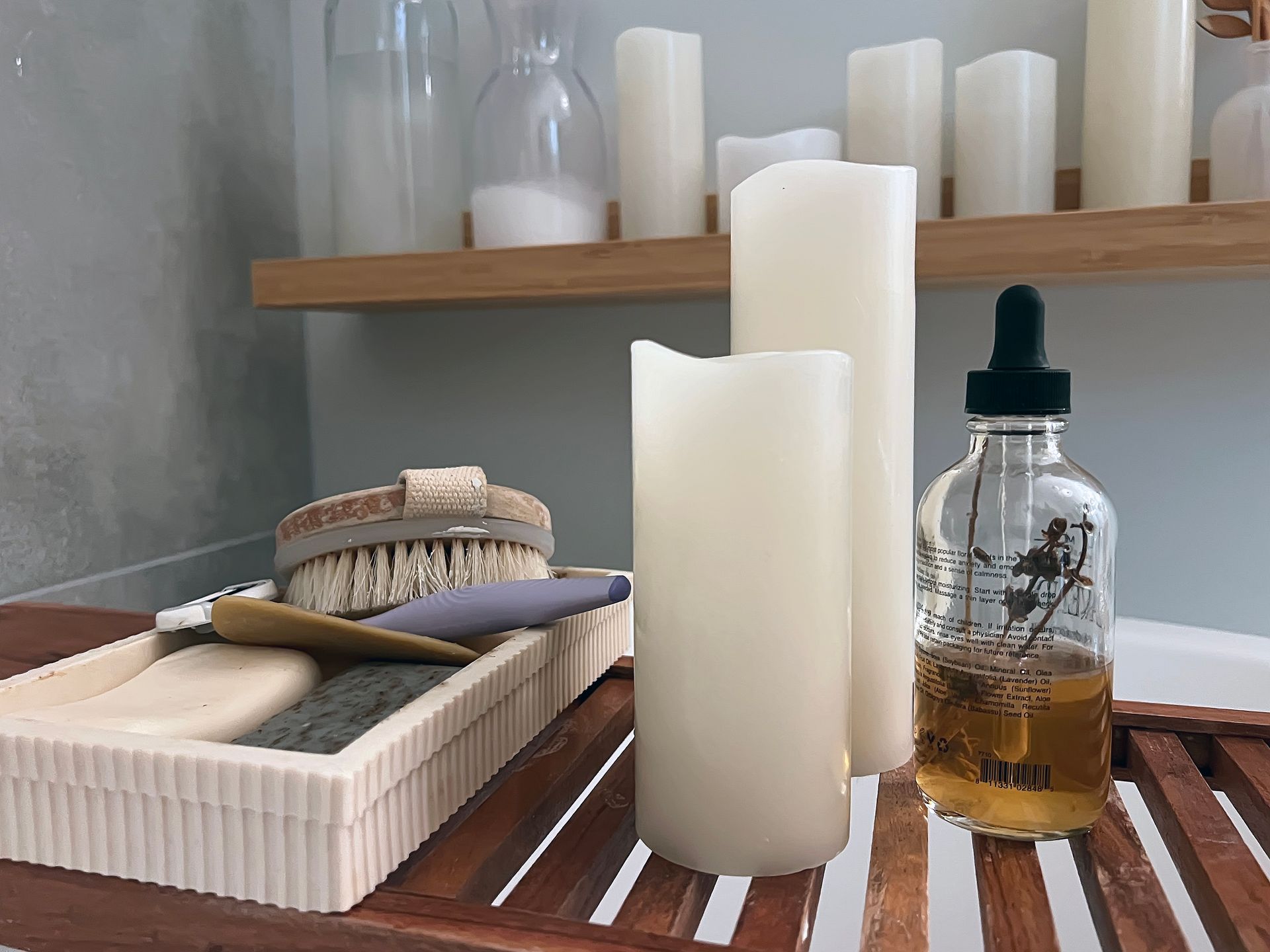 Spa shelf with white candles, wicker brush, and glass amber bottle on a wooden tray