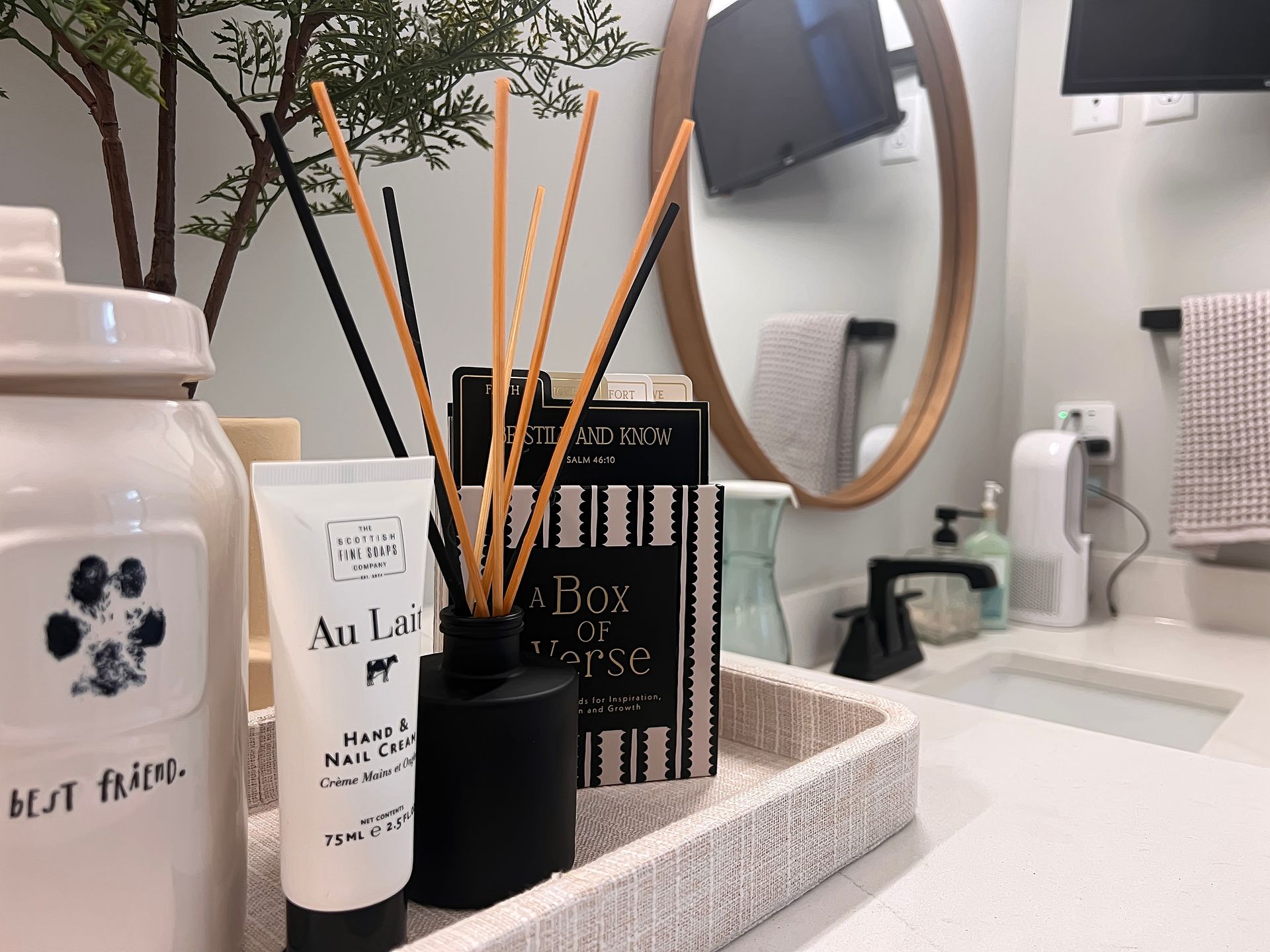 Bathroom vanity tray with toiletries, reed diffuser, and a mirror sink in the background
