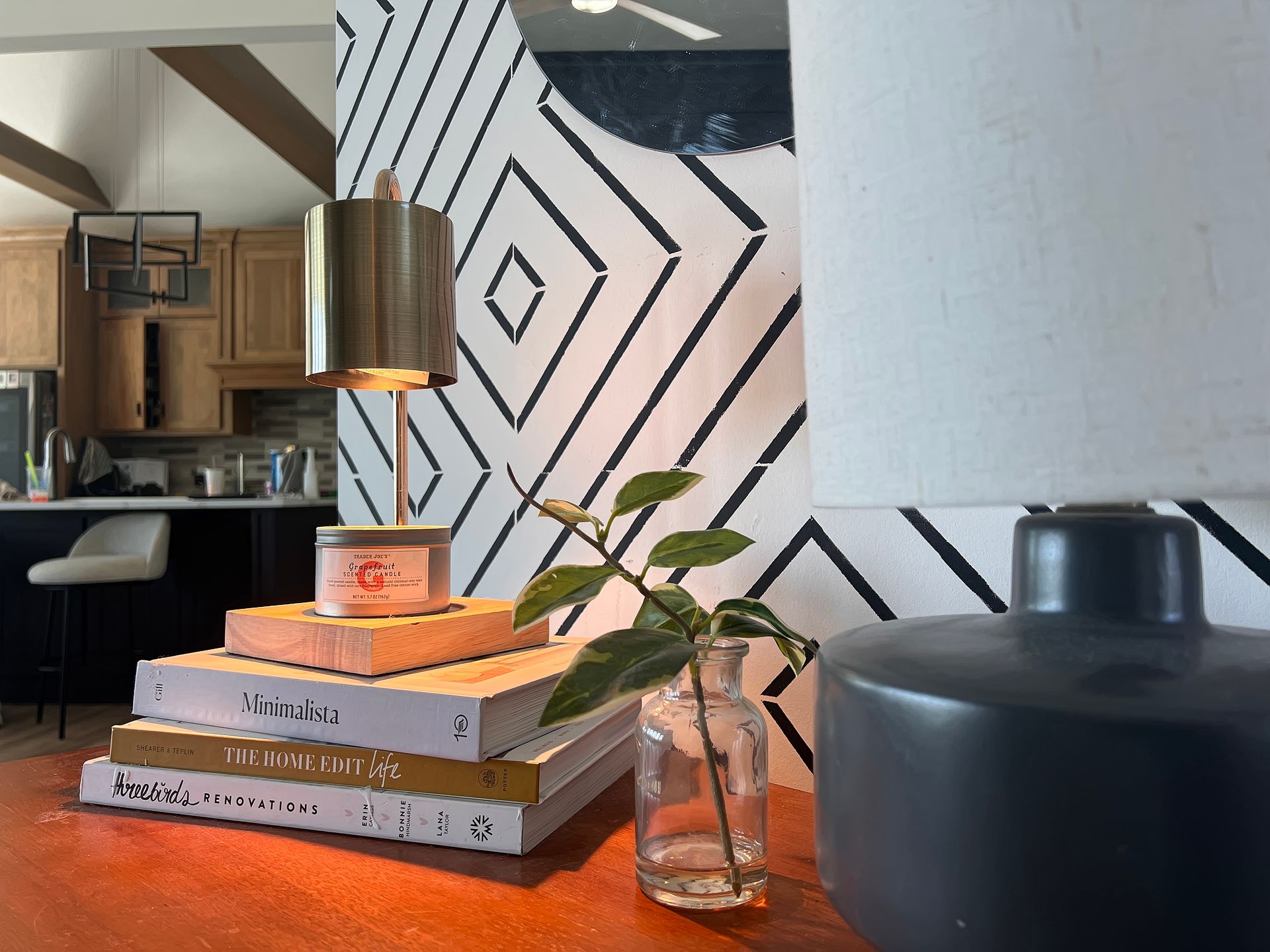 Modern living room shelf with books, a small plant, candle, and black vase against geometric wall art