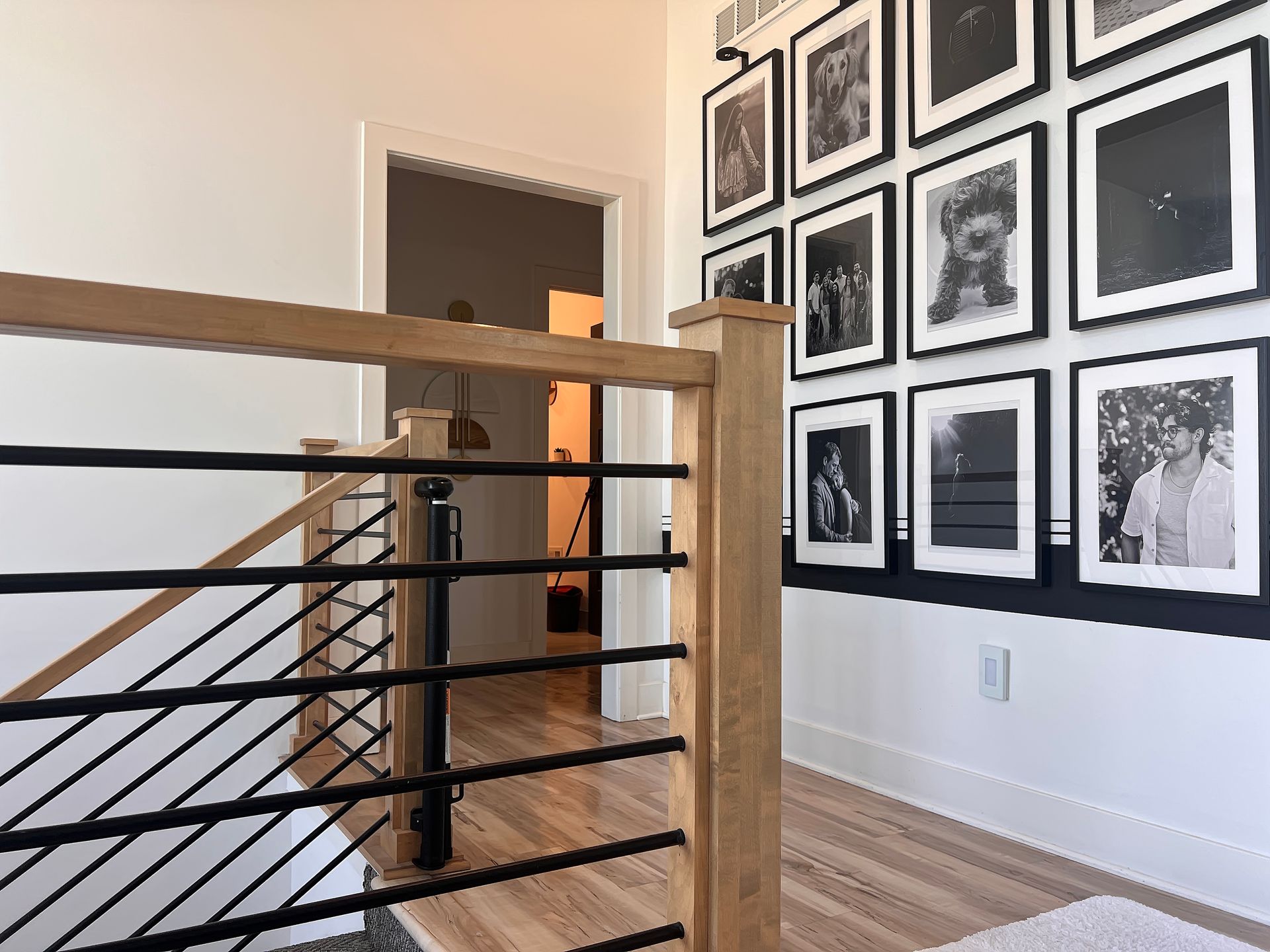 Modern indoor stair railing with wood posts, black cable rails, and framed black-and-white art on the wall.
