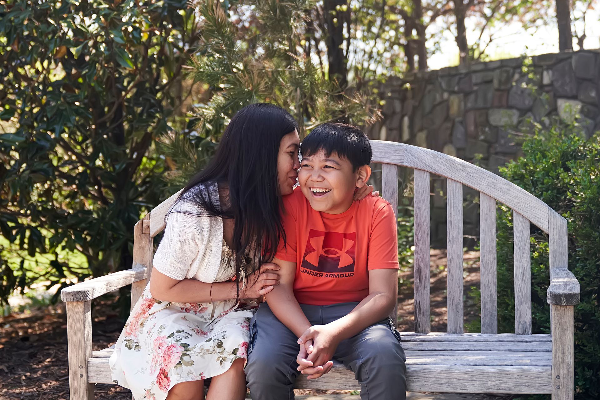 Mother and son laughing on a white bench in a sunny garden