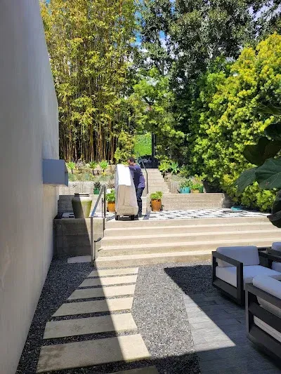 Person pushing a dolly with a large box up outdoor stairs. Stone patio, trees in background.