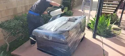 Person wrapping a large item with plastic wrap outdoors.