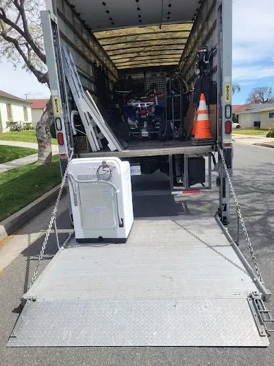 A moving truck with its ramp down, a white washing machine, and other items being loaded.
