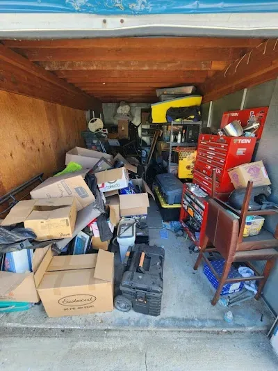 Storage unit filled with boxes, tools, and other items, appearing cluttered.