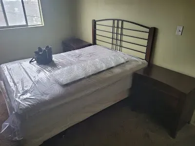 Bedroom with a bed, two nightstands, and a window. The bed is covered in plastic wrap.