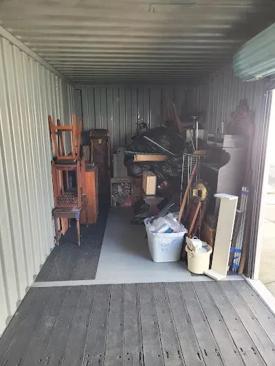 Storage unit filled with furniture and miscellaneous items; wood floor, metal walls.