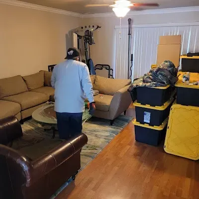 Man in light blue shirt walks in living room with furniture, boxes.