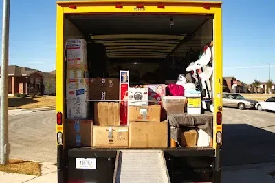 Inside of a yellow moving truck, filled with packed boxes and household items, ramp down.