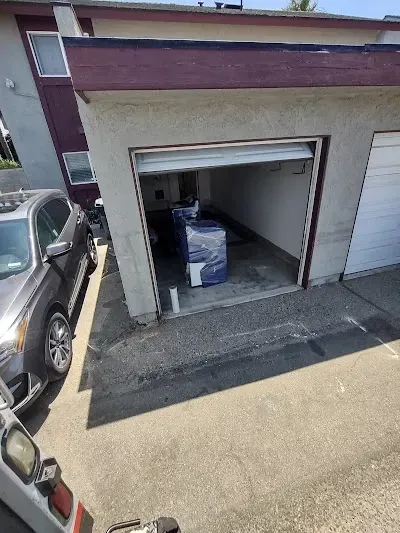 Garage with partially open door; furniture wrapped in blue plastic inside, gray car parked outside.