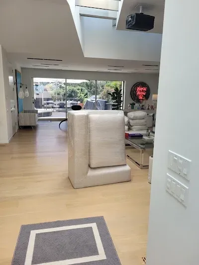 A couch wrapped in protective material sits in a bright room with hardwood floors and large windows.